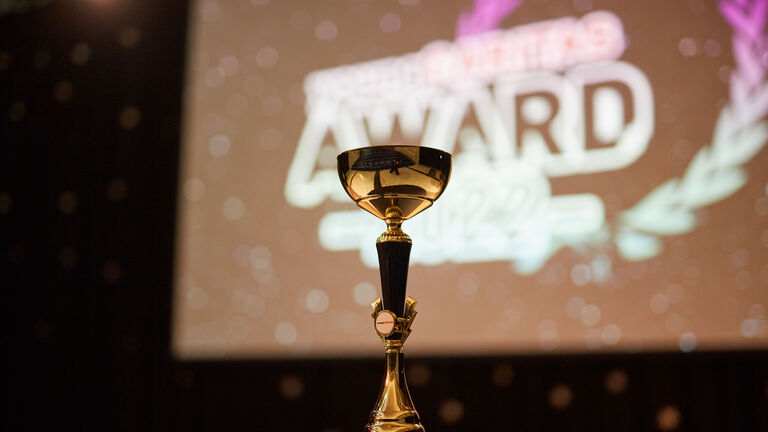 Pokal vor Leinwand auf der das youngCaritas-Award Logo zu sehen ist. 