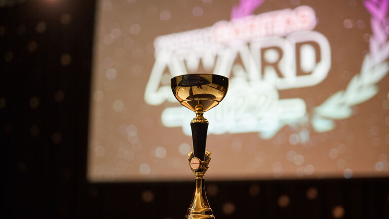 Pokal vor Leinwand auf der das youngCaritas-Award Logo zu sehen ist.